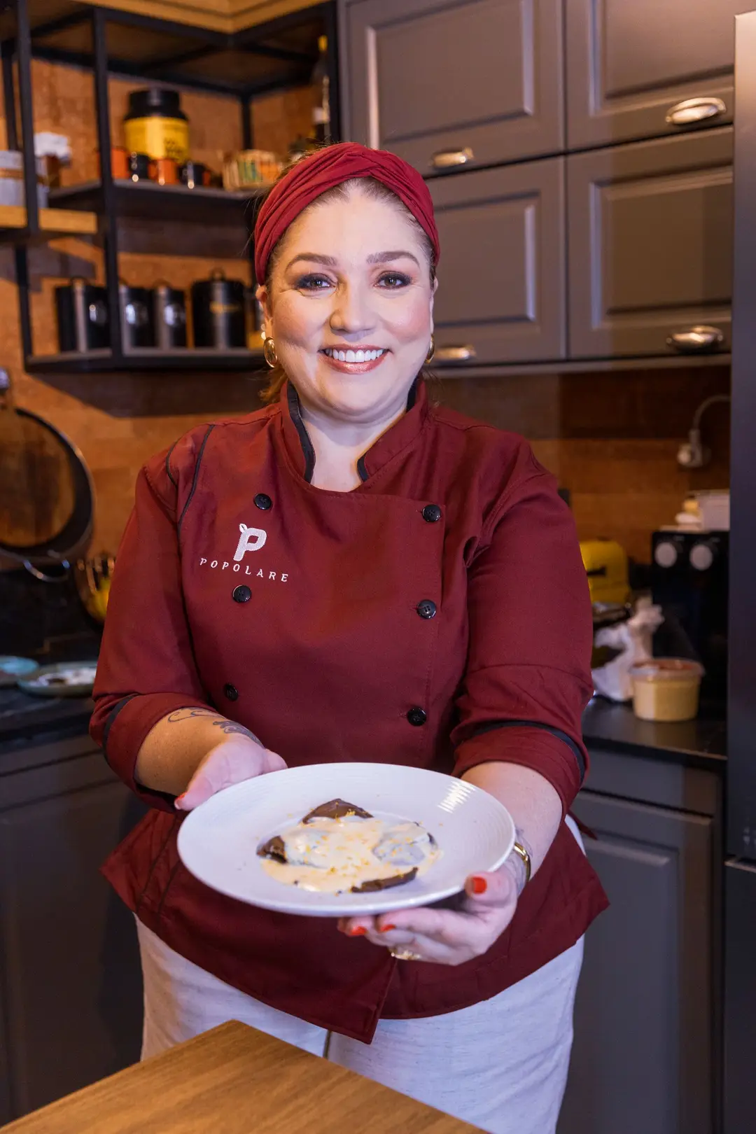 Carina Popolare, de dólmã marsala, mostrando um prato de massa recheada na cozinha