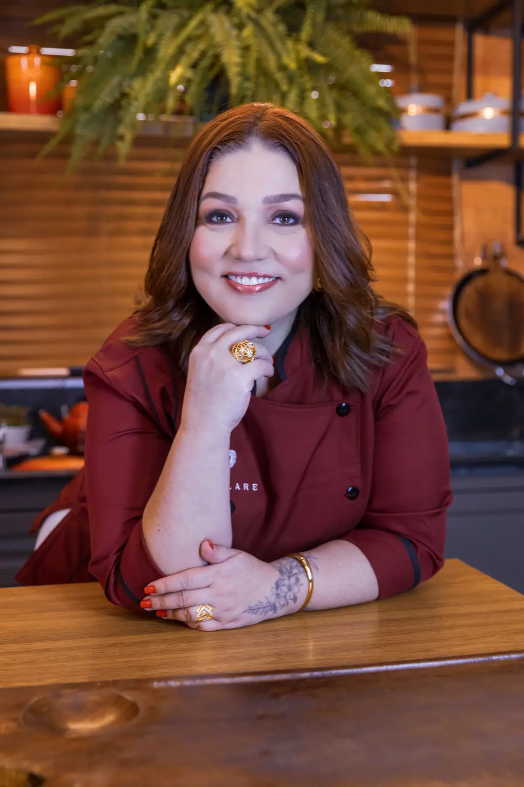 Carina Popolare, de dólmã marsala com o logo da Popolare, sorrindo apoiada na bancada da cozinha